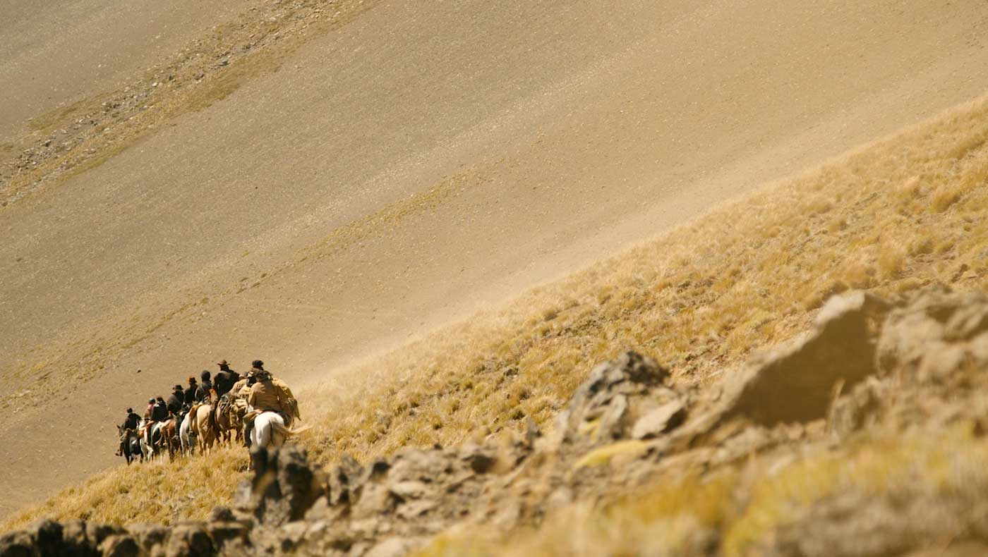 Hats down against the fierce winds, the riders push past blowing sand towards the valley beyond.